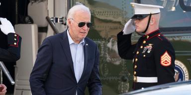 En bild på USA:s president, Joe Biden, på väg ut ur en grön militärhelikopter och på väg motl en bil. Han är iklädd marinblå kostym. ljusblå skjorta och han bär pilotglasögon. Till höger om presidenten syns en uniformsklädd man som gör honnör.