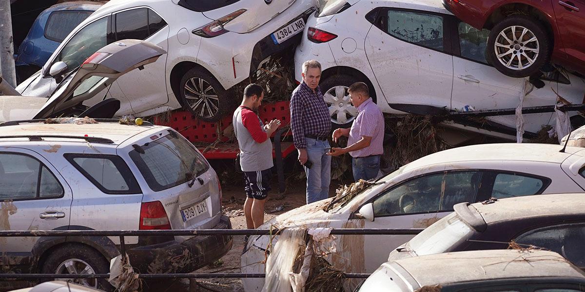 En bild som visar resultatet av översvämningar i Spanien. Bilar som dragits med av vattnet ligger huller om buller och i mitten syns några människor.