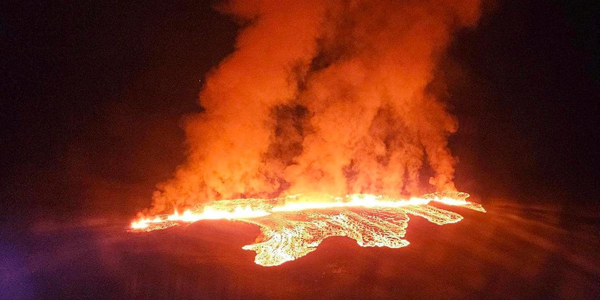 Het lava och rök kommer från en vulkan som har utbrott på Island. Bilden är tagen när det är mörkt och den orangea glödande lavan lyser upp röken och det svarta berget.