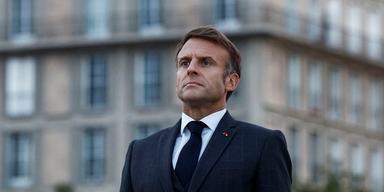 En halvbild på Frankrikes president, Emmanuel Macron, iklädd marinblå kostym och mörkblå slips. Han har en allvarlig min och står rakt i ryggen. Bakom honom syns en gråaktig klassisk byggnad med många fönster.