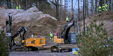 Bild på en byggarbetsplats med grävskopor, borriggar, grävmaskiner, baracker och byggarbetare.