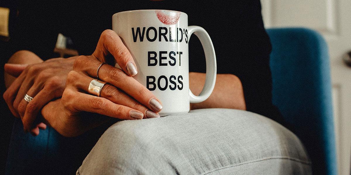 En kvinna sitter med en kaffemugg i knät. På muggen står det "Worlds Best Boss".